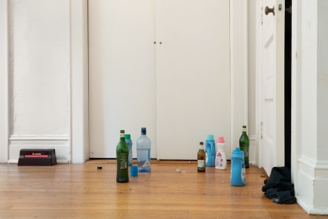 A photograph of bottles of detergent and liquor on the ground with a rat trap at left