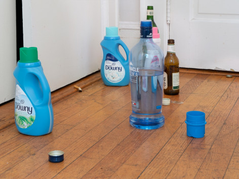 A photograph of detergent and liquor bottles on the ground with a smoked cigarette