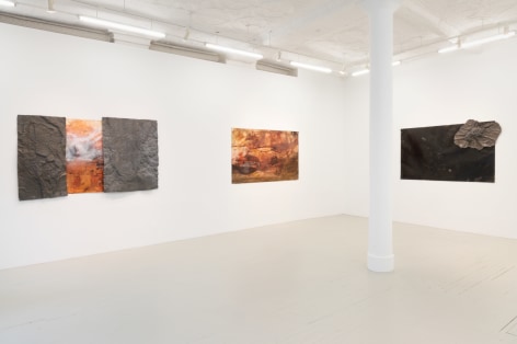 three paintings hanging on the wall where both works have orange brown and white colors in gestures that look like tumultuous sea scapes and the painting on the left has textured metal components attached to the surface, and the third painiting is solid black with a small metal sculpture attached to the upper right corner