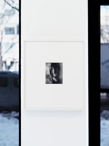 A photograph framed in white on a skinny white wall. The small black and white photograph, 1/4 the size of the frame, seems like two lips smacking against one another.