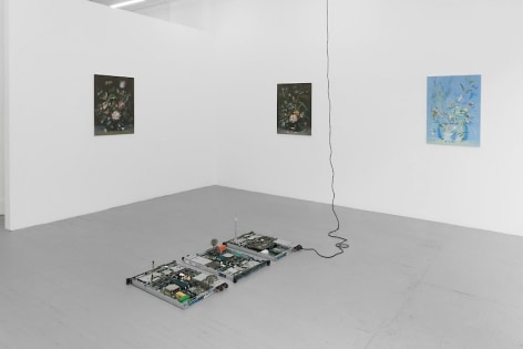 A photograph of the gallery with 3 paintings on the front wall, and a circuit board sculpture on the ground. The 2 paintings at left are black with color. The painting at right is in tones of blue and green.