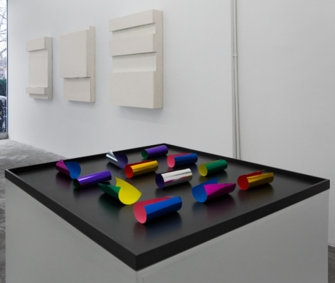 A photograph of a sculpture on a pedestal, with 3 works on a wall in the background