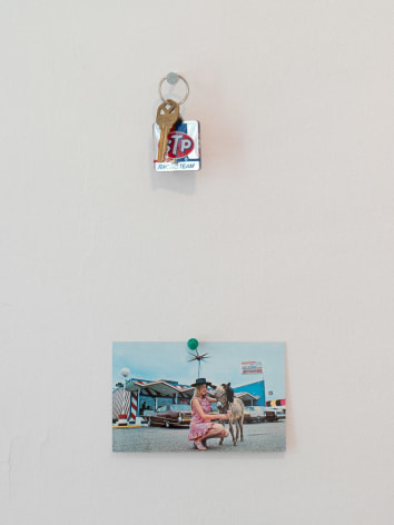 A close-up photograph of a key chain tacked to the wall and a postcard attached with a pin