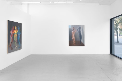 A photograph depicting two large paintings: one with three figures standing together, painted in red, yellow, and blue; the other with a single female naked body flattened like a paper doll, folding over herself, with an identical grey silhouette to the right of her. We see the gallery's front window at right.