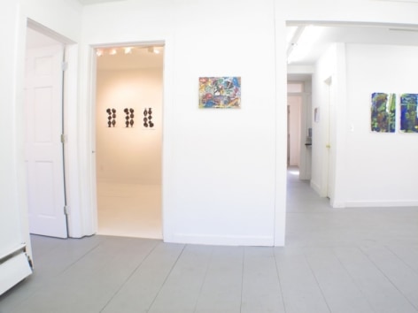 A photograph of the interior of the gallery: 3 image are in a separate room in the background, one is on a wall in the foreground, and at right we see 2 works partially
