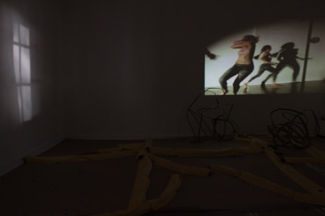 A photograph of a video projection, the room is otherwise dark. On the ground are barely visible sculptures.