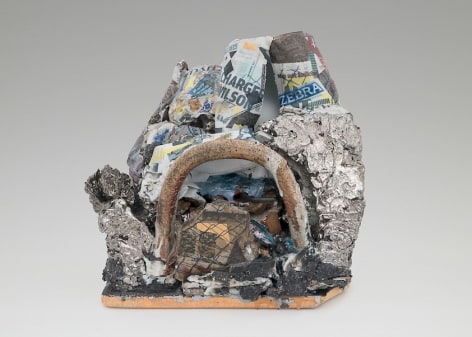 A mixed stoneware sculpture with a central arc made of stone. There textured surfaces surrounding it are painted with silver luster. Above those elements are varied jagged surfaces that host decals applied by the artist of newspaper articles and a chainlink fence print.
