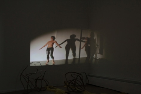 A photograph of a video projected onto a wall. The room is dark, there is an object in the foreground that is illegible