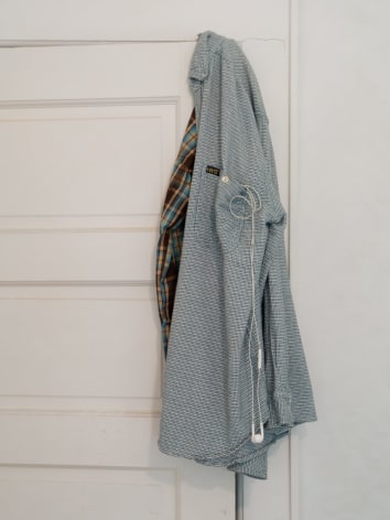 A close-up photograph of the shirt over the white door with headphones coming out of the pocket