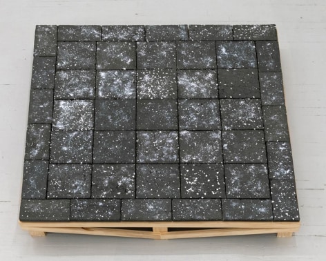 A sculpture of 45 black clay tiles on a wooden pedestal