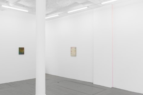 A photograph of the gallery that includes 2 Monick paintings in the background on 2 walls perpendicular to one another. On the right wall, there is also a pink ribbon artwork installed in the corner.