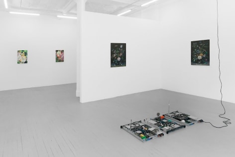 A photograph of 4 paintings on 3 walls, and a sculpture of circuit boards on the ground.