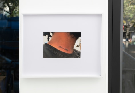 color photograph in a white frame showing the neck of a person who looks to be male with a beard and dreadlocks. The phrase &quot;Yes, I know&quot; is tattooed on his neck.