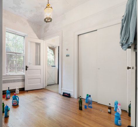 A photograph of the room with detergent bottles and liquor on the ground, open, and a shirt on the door at right