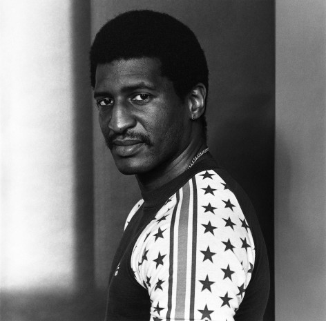 Man looks over his left shoulder at the viewer. He is wearing a t-shirt with stars and stripes.