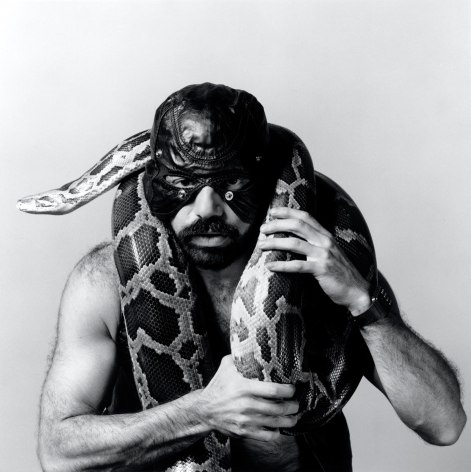 Man wearing leather mask, holding snake.