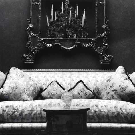 Patterned couch, centered, with mirror on wall behind and table with glass object in front.