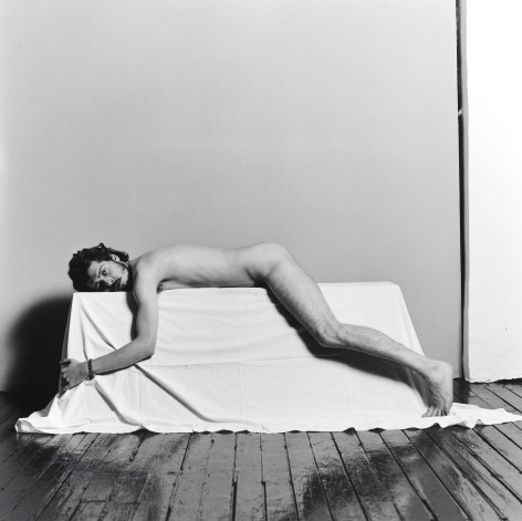 Nude white male laying prone on a white cloth box.
