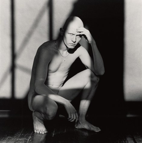 A man crouching in an interior, a geometric shadow is cast over his body.