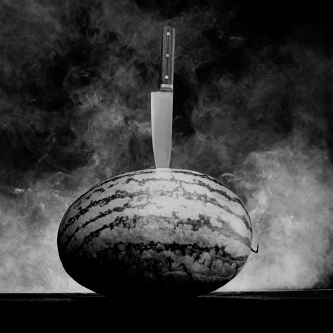 Full watermelon with knife stuck in center.