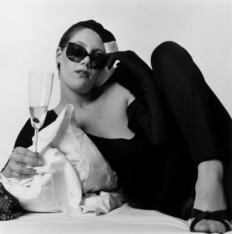 Portrait of white woman on bed holding champagne.