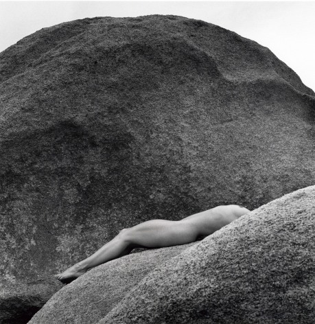 Lisa Lyon lying on rocks nude back is ached and head is hidden.