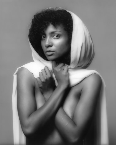 Nude woman from the waist up holding a white piece of fabric around her like a hooded cape.