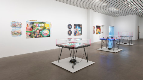 Installation of The Founder's Paradox at MCA Cleveland in 2018, featruing several tables with boardgames on them and covered in Plexi galss in the senter of the room and several large works on the wall that look like covers from board games.