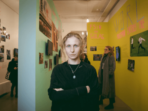 Woman standing in front of an art gallery installation of many pictures and photographs hung salon-style