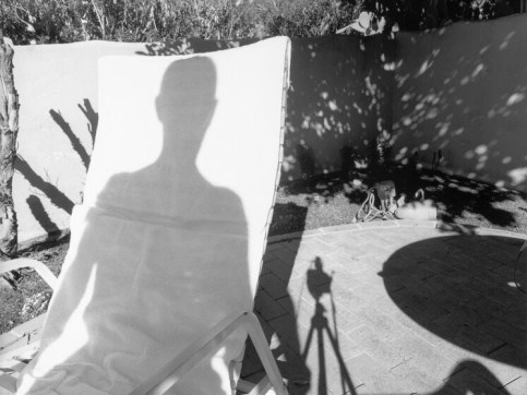 Black and white photograph of an outdoor patio, with shadow cast on a chair by the male photographer