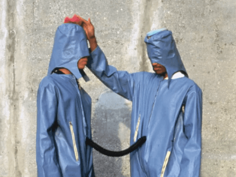 Two people wearing light blue jumpsuits and hoods as part of an artwork