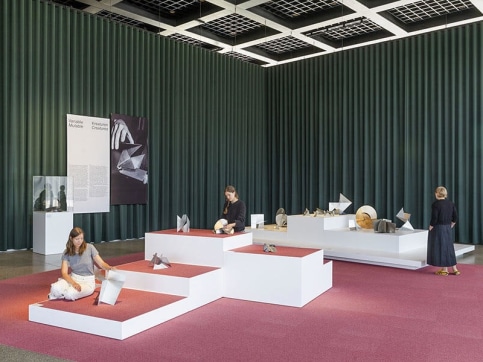 Museum installation of sculptures on top of white plinths with pink carpeting and green curtains