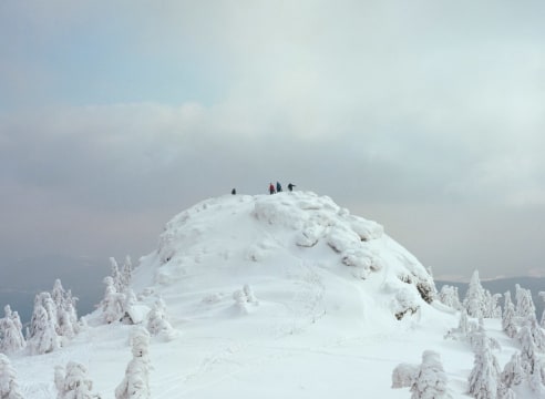 Photo of hikers on top of a small mountain covered in show, seen from a distance.