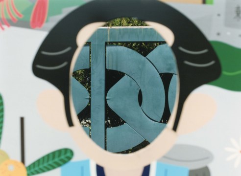 Color photograph of a cut out Japanese cartoon face, showing the fence behind.