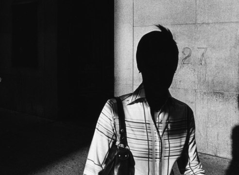 Black and white photo of a woman on a sidewalk, her face is silhouetted in shadow.