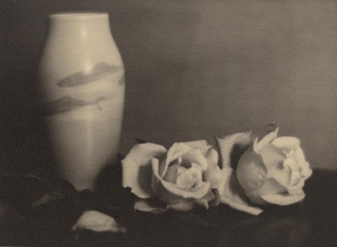 Black and white photo of a vase decorated with Japanese Koi, two white roses are sitting to the right to the vase.