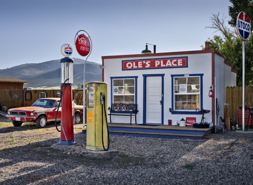 Color photograph of an old fashioned gas station with a vintage red Mustang parked in the background