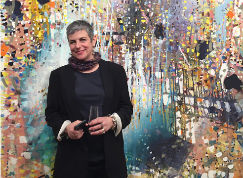 picture of Jackie Saccoccio standing in front of one of her multi-colored abstract paintings 