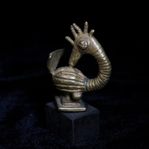 Small gold sculpture of a cartoonish bird with prominent carved stripes. Its eye resembles a button and it has a crown of feathers on the top of head which are small and cylindrical. 
