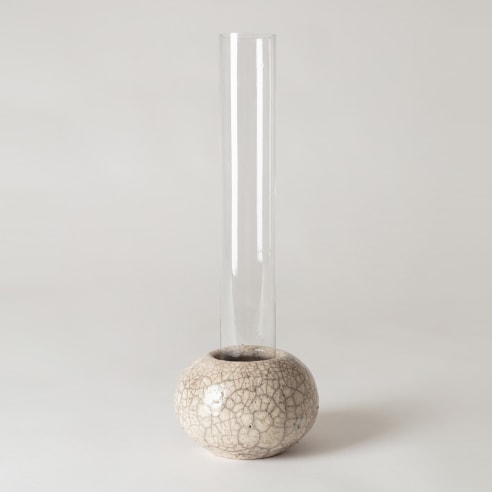Clear tall glass tubular vase sitting inside raku ceramic holder. 