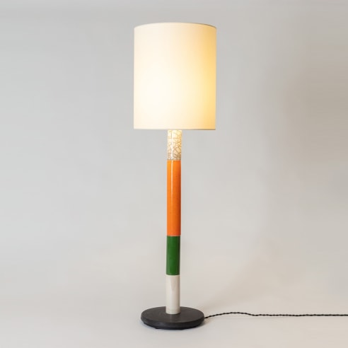 Floor lamp in various colors, white fabric shade. Colors from bottom to top, black base, white section, green section, orange, white raku. Light turned on. 