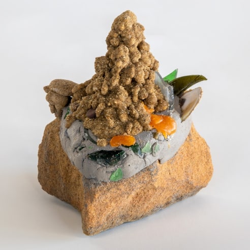 a sculpture by Lily Cox-Richard of a dribbled sand castle on a stone with broken glass shards around its edges