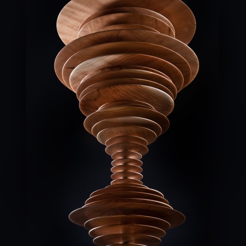 close-up view of a totemic wood sculpture by Elizabeth Turk featuring thin discs layered on each other to resemble a sound wave