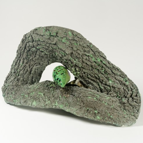 a sculpture by Lily Cox-Richard of cast tree bark with a green tongue-like form emerging from a knot in the center