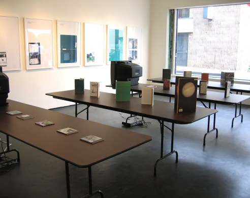 Library installation view, books and tv's set up on tables
