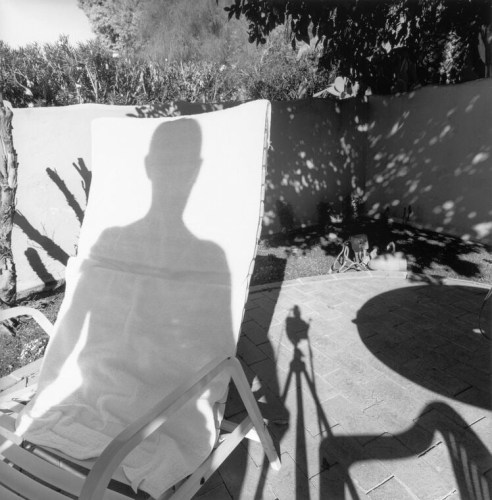 Black and white photograph of an outdoor patio, with shadow cast on a chair by the male photographer