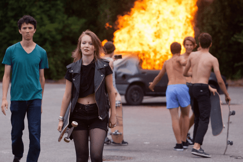 Teenagers with skateboards in front of a burning car