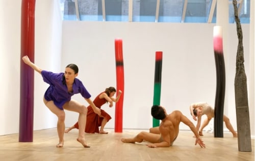 4 dancers interacting with vertical sculptures in an art gallery