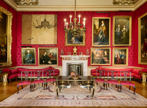Blenheim Palace sitting room with multiple portrait paintings hung on red walls