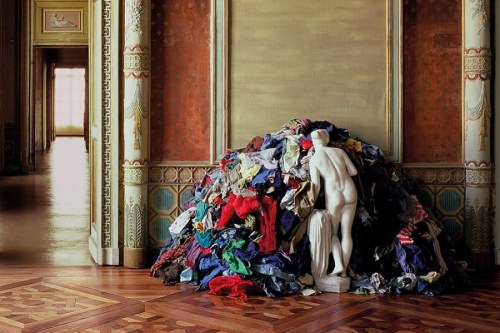 Plaster sculpture of a nude woman facing a mound of multi-colored rags